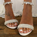 White sandals with pearl embellishments on a wooden surface.