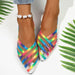 Multicolored strappy shoes worn with a white background and green leaves.