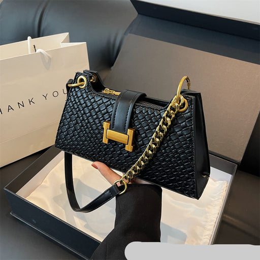 Black handbag with gold chain and hardware held by a hand, with a 'THANK YOU' bag in the background.