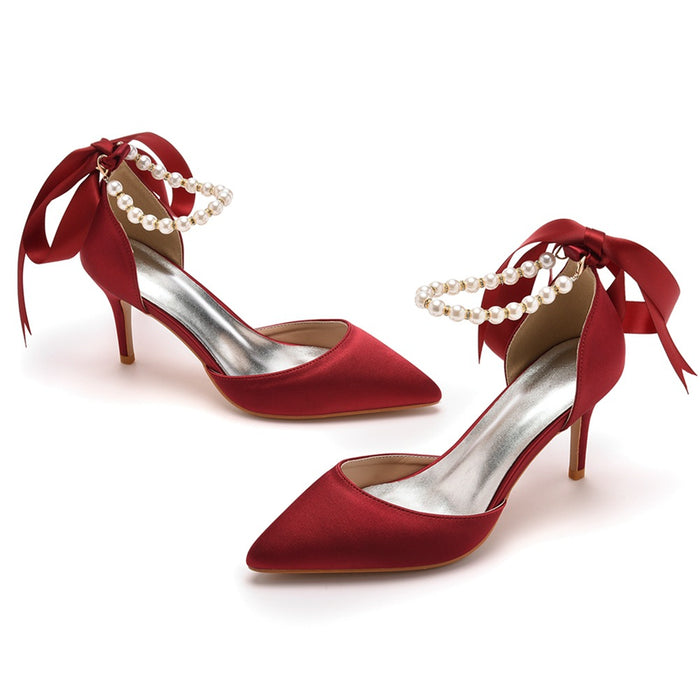 Red high-heeled shoes with pearl anklets on a white background