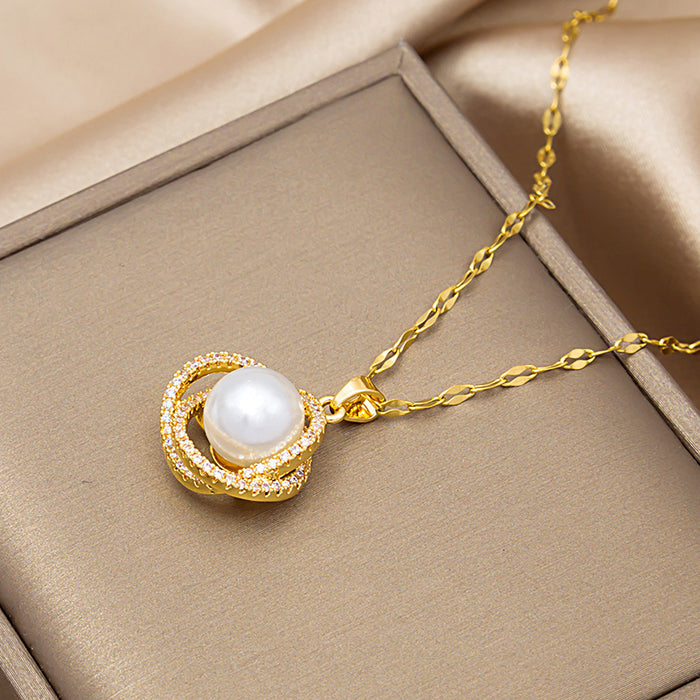 A gold pendant necklace with a white pearl and small clear stones, displayed on a beige jewelry box.