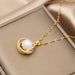 A gold pendant necklace with a white pearl and small clear stones, displayed on a beige jewelry box.