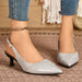 A pair of women's pointed-toe slingback pumps in textured silver faux leather with black kitten heels, shown on a model wearing blue jeans and a gold chain anklet.