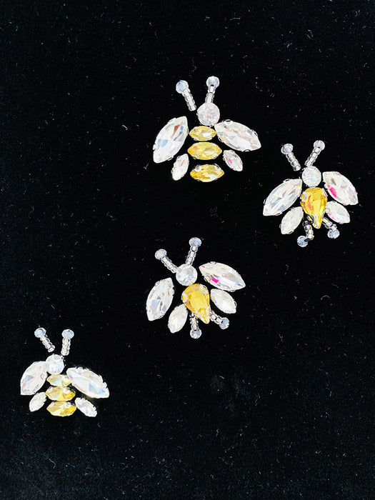 Four bee-shaped pins with yellow centers and clear gemstones on a black background