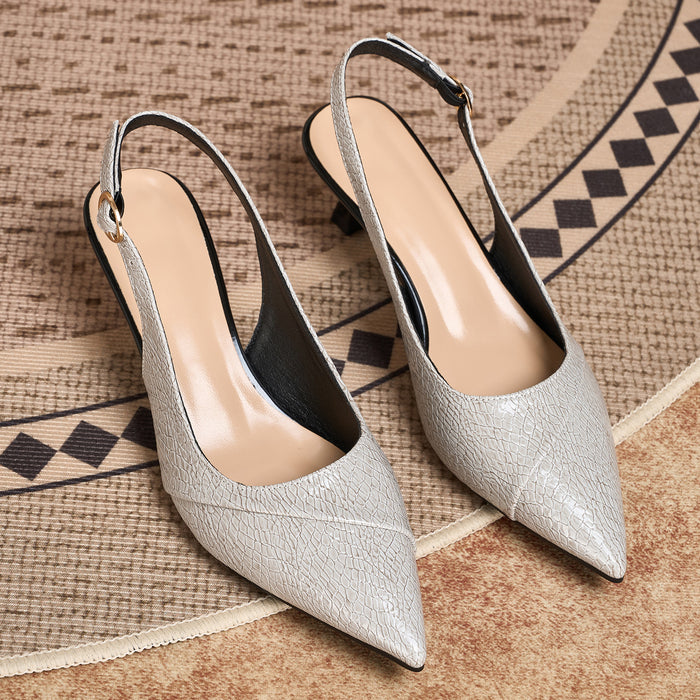A pair of pointed-toe slingback pumps in a textured metallic silver finish, displayed on a woven rug.