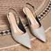 A pair of pointed-toe slingback pumps in a textured metallic silver finish, displayed on a woven rug.