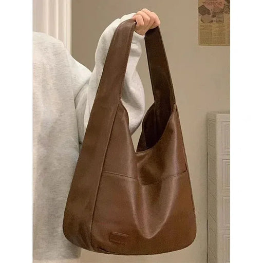 Brown leather handbag held by a person wearing a light gray sweater.
