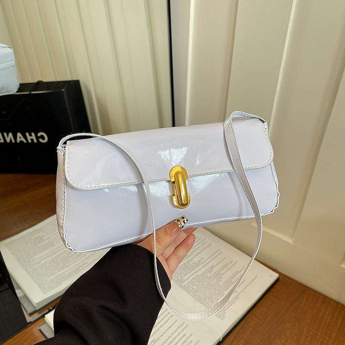 White handbag with gold clasp held by a person, with a blurred background