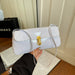 White handbag with gold clasp held by a person, with a blurred background