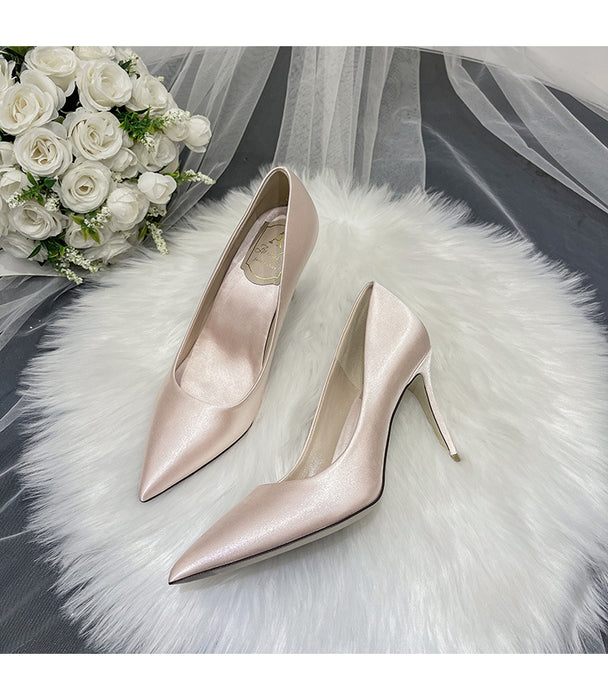 Pair of pink high-heeled shoes on a white fur surface with a bouquet of white roses in the background.