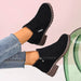 Black suede ankle boots worn with light blue jeans on a pink background