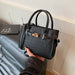 A black crocodile-embossed leather handbag with gold-tone hardware, held by a person's hand while resting on a dark gray leather sofa next to a book.