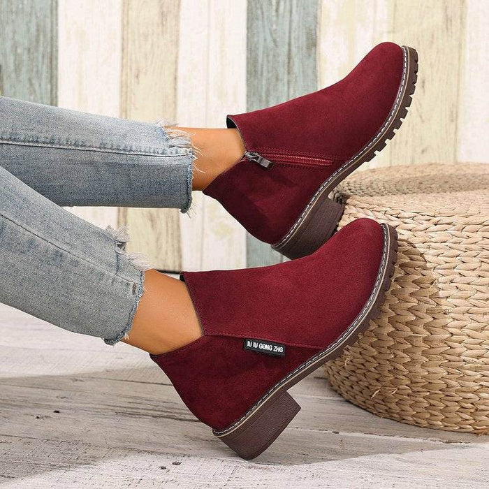 Red ankle boots worn with light blue jeans on a wooden floor.