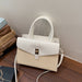 A structured handbag in off-white and cream, featuring a smooth faux-leather flap top with a gold-tone clasp, a woven lower body, dual top handles, and a detachable shoulder strap, resting on a wooden floor against a plain wall.