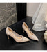 Pair of beige high-heeled shoes on a dark surface with a marble wall in the background.