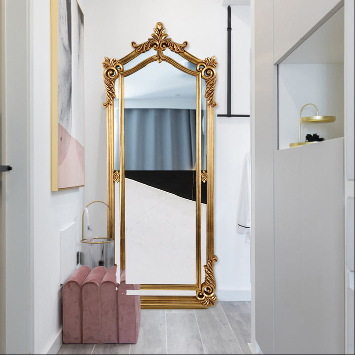 Decorative gold-framed mirror in a room with a pink chair and white walls.