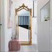 Decorative gold-framed mirror in a room with a pink chair and white walls.