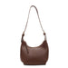 A brown leather shoulder bag with a crescent-shaped body, a single adjustable strap, and a small hanging leather tag, shown against a plain white background.