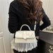 A woman wearing a black long-sleeve top and a white pleated ruffled skirt carries a small white top-handle handbag over her shoulder in an indoor setting.