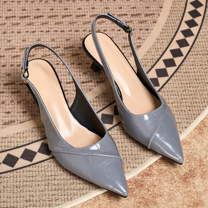 A pair of women's pointed-toe slingback pumps in a glossy light gray faux-croc leather, displayed on a textured beige and black patterned rug.