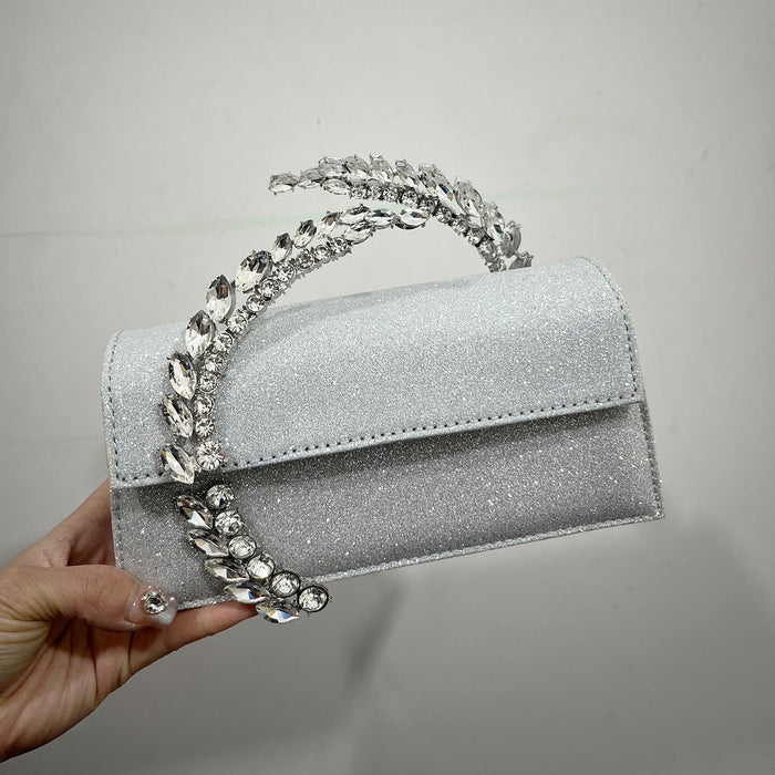 Silver glittery handbag with decorative handle held by a hand against a gray background