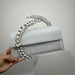 Silver glittery handbag with decorative handle held by a hand against a gray background