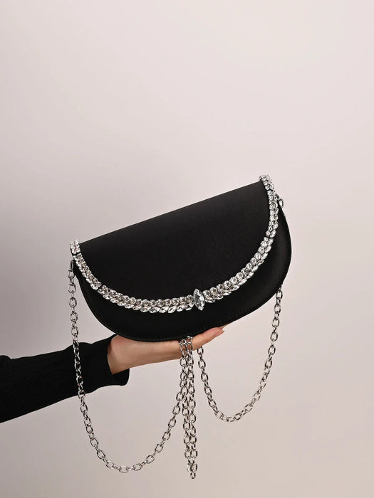 Black clutch with silver chain held by a hand against a neutral background