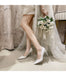 White high-heeled shoes worn with a wedding dress and bouquet.