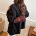 Person wearing a black coat with a burgundy handbag featuring a gold clasp.