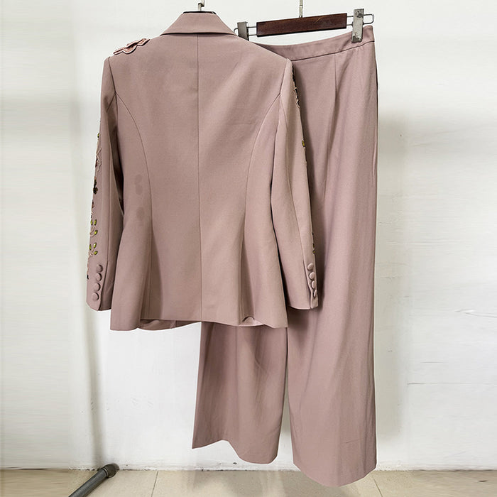 Pink suit jacket and pants on hangers against a white wall.