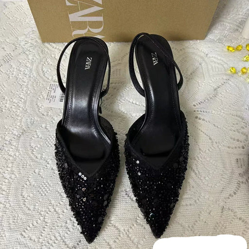 Black high-heeled shoes with sequin details on a textured surface, with a box in the background.