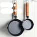 Two small frying pans with wooden handles hanging on a white tiled wall.