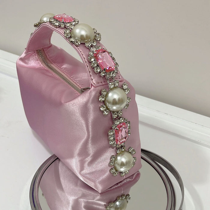 Pink handbag with pearl and gemstone embellishments on a white surface.