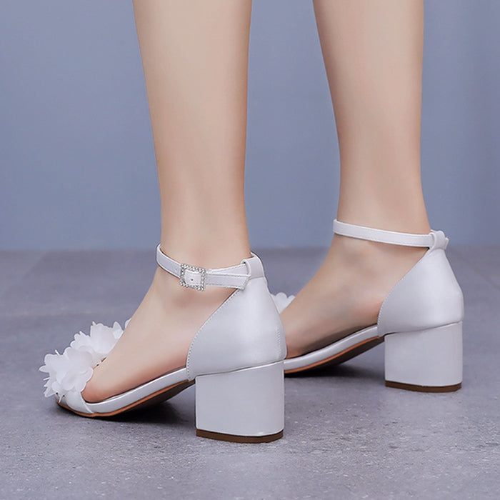 White high-heeled shoes with floral details on a gray background