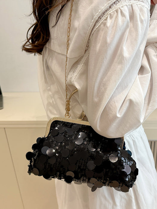 A person wearing a white puff-sleeve dress carries a black sequined kiss-lock clutch bag with a gold-tone chain strap and frame.
