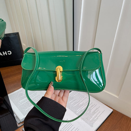 Green handbag with gold clasp held by a person on a wooden surface.