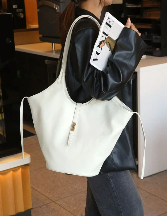 Person holding a white tote bag with a magazine, standing in an indoor setting.
