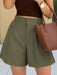 Person wearing olive green shorts and a brown top, holding a brown handbag.