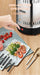 A countertop food warmer or steamer with a clear lid and black base, shown on a wooden table with a hand pressing a red button. Text at the top reads 'ONE-BUTTON OPERATION.
