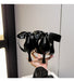 Black high-heeled shoes with large bows held by a person against a neutral background