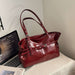 A glossy deep red leather handbag with double shoulder straps and silver-tone hardware, styled on a light-colored fabric-covered surface next to an open laptop.