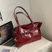 A glossy deep red leather handbag with double shoulder straps and silver-tone hardware, styled on a light-colored fabric-covered surface next to an open laptop.