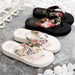 Pair of black and white flip-flops with floral straps on a stone surface.