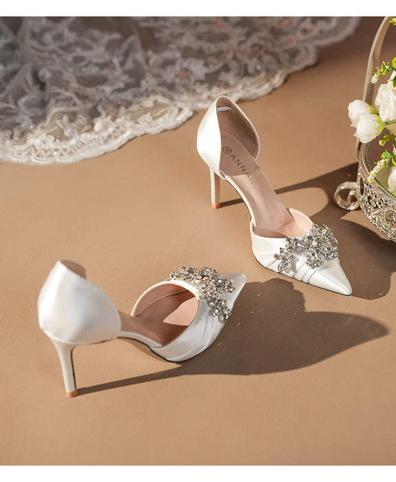 White high-heeled shoes with embellishments on a beige surface
