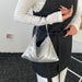 A person wearing a white long-sleeve top and a black apron-style garment holds a silver sequined slouchy shoulder bag with thin metallic handles.