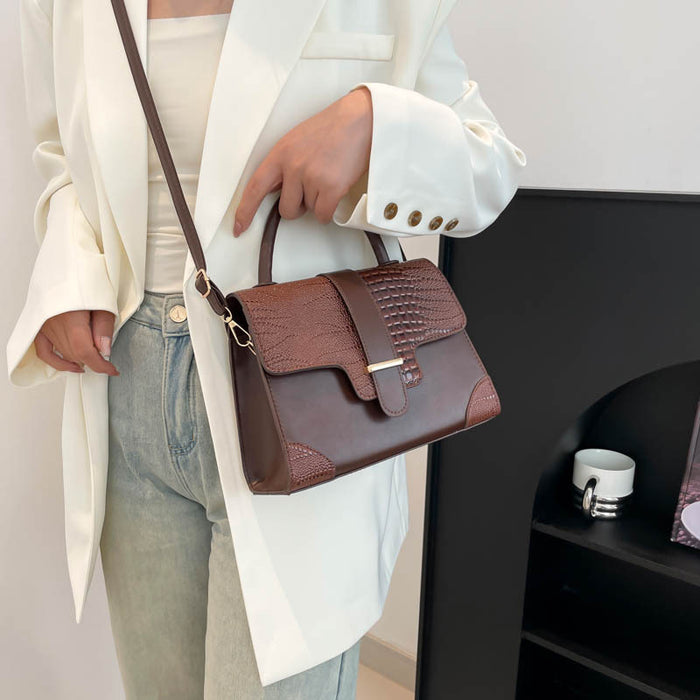 A woman wearing a white blazer and light blue jeans carries a brown leather handbag with a top handle and shoulder strap. The bag features a smooth front panel, a crocodile-embossed flap, and gold-tone hardware.