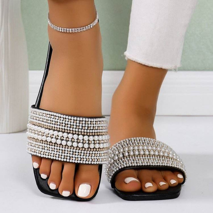 Black sandals with pearl embellishments worn by a person on a white background