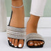 Black sandals with pearl embellishments worn by a person on a white background