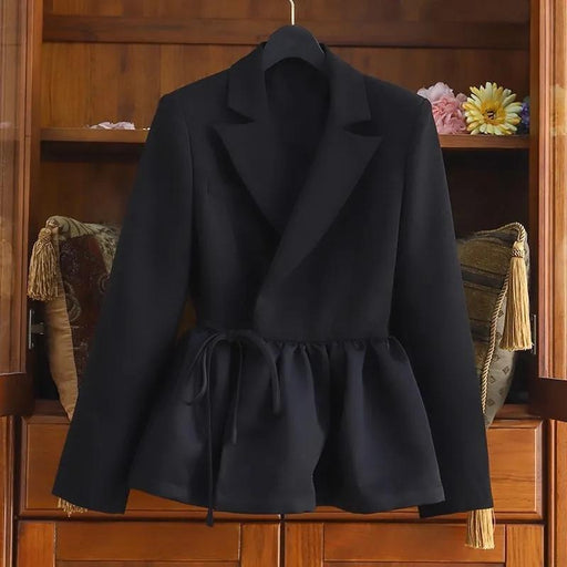A black long-sleeve wrap-style blazer with a peplum waist and drawstring tie, displayed on a hanger against a wooden cabinet background.