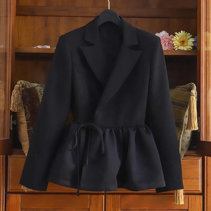 A black long-sleeve wrap-style blazer with a peplum waist and drawstring tie, displayed on a hanger against a wooden cabinet background.